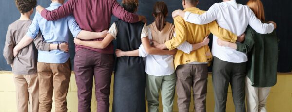 A group of nine people standing in front of a blackboard with their arms around each other''s shoulders, representing unity and togetherness.